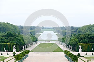 A lonely view of Versailles park, France. The geometrical combination of green trees, grass areas and white statues.