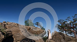 Lonely wedding couple stands on the rocks under deep blue sky
