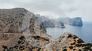 Lonely white Car on serpentine curved asphalt mountain road near Lighthouse of Cap de Formentor rocky coast. Mallorca Island,