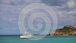 Lonely white luxurious sailboat, yacht in Caribbean ocean harbor near the rock.