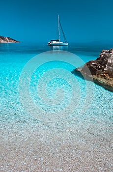 Lonely white sailing catamaran boat drift on calm sea surface. Pure azure clean blue lagoon with shallow water and