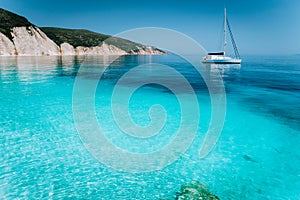 Lonely white sailing catamaran boat drift on calm sea surface. Pure shallow azure blue bay water of a beautiful beach