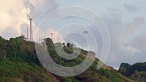 A lonely wind power generator standing on a mountain in a thicket of trees against a background of blue sky and beautiful cumulus