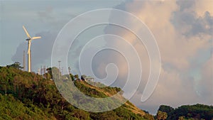 A lonely wind power generator standing on a mountain in a thicket of trees against a background of blue sky and beautiful cumulus