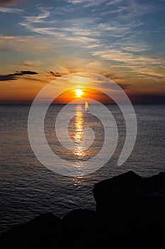 Lonely Wind surfer setting sail towards the dramatic and magnificent scenic sunset at the coast of the mediterranean sea in