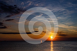 Lonely Wind surfer setting sail towards the dramatic and magnificent scenic sunset at the coast of the mediterranean sea in