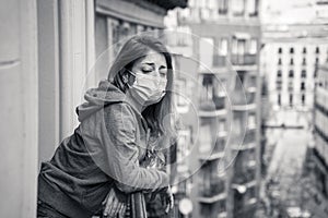 Lonely woman with face mask in quarantine feeling sad and hopeless looking outside in home balcony