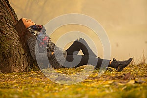 Lonely woman having rest under the tree near the water in a foggy autumn day