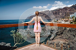 Lonely woman with long braid stands on viewpoint with ocean landscape Los Gigantes cliifs. Rocky coastline. Deep blue