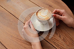 Lonely woman with nice manicure in warm wood sweater drinking coffee in the morning, top view of female hands holding cup of hot