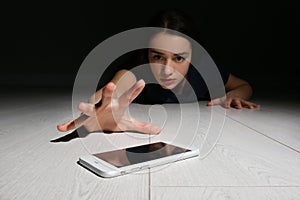 Lonely woman reaching out for smart phone on floor indoors