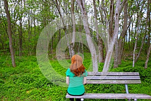 Lonely woman rear view looking to forest sitting on bench