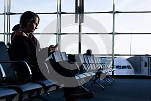Lonely woman seating at airport terminal looking at cellphone