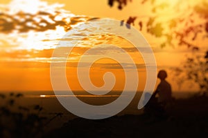 A lonely woman sits on the rock and enjoys the sunset