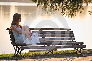 Lonely woman sitting alone on lake shore bench on warm summer evening. Solitude and relaxing in nature concept