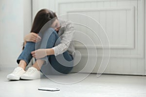 Lonely woman sitting on floor and smartphone on foreground