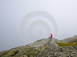 A lonely woman sitting on the top of a mountain looking at the horizon on a foggy summer day