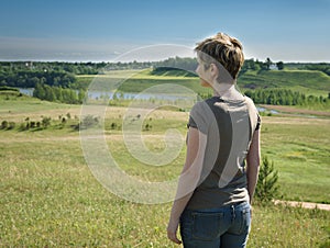 Lonely woman standing with her back on green field