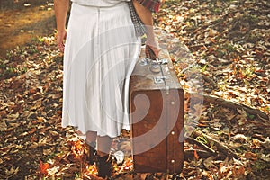 Lonely woman with a suitcase walking in the forest an autumn day