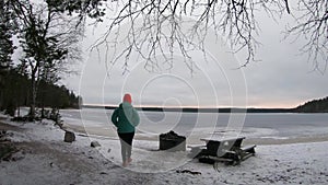 Lonely woman traveler wearing a winter jacket and red cap walking towards the frozen lake