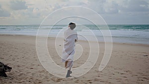 Lonely woman walking beach on cloudy day. Calm tourist watching ocean waves rear