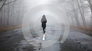 Lonely woman walking in fog. Rural landscape with road in morning mist. Warm autumn colors. Dark mysterious background