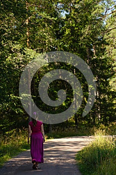 A lonely woman walks away along a dirt road along the forest. Vertical photo, freedom concept