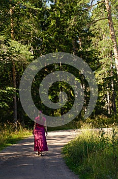 A lonely woman walks away along a dirt road along the forest. Vertical photo, freedom concept