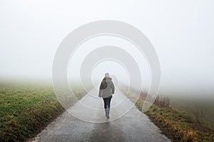 Lonely woman walks on empty road in fog