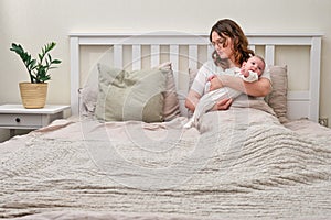 A lonely woman with a newborn baby is lying alone in an empty bed. Mom with a child in her arms in the bedroom