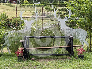 The lonely wooden bench in the flower garden and decorated by the deer standee
