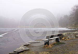 Lonely wooden bench in winter scenery by frozen lake in foggy rainy weather, bergen, norway