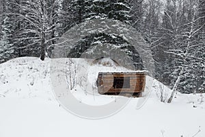 A lonely wooden building with a pile in a dense forest, winter time a snow hut