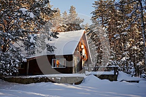 Lonely wooden log house among a winter pine forest, large snowdrifts around, a clear sunny day, snow on the branches of trees