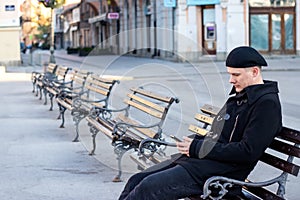 Lonely or worried young man sitting alone on a bench in empty public square.