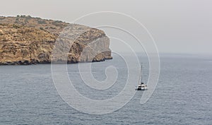 Lonely yacht floating by steep cliff