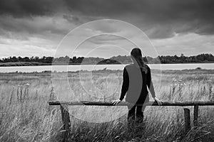 Lonely young depressed sad woman sitting on a wooden beam or fence glazing into the distance. Monochrome portrait.