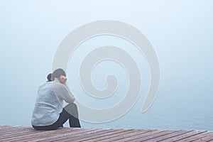 Lonely young depressed woman sitting on a wooden stage on a foggy day. Depression concept.