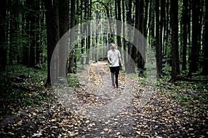 Lonely young male hipster in casual walks in autumn dark moody forest with fallen leaves