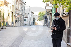 Lonely young man with protective mask on face, standing alone in empty public square.