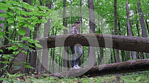 A lonely young woman in a plaid shirt walks along a fallen tree in the forest. The girl enjoys a walk in the forest.