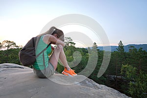 Lonely young woman sitting depressed on hillside trail on warm summer evening. Lost female hiker crying on rocky cliff