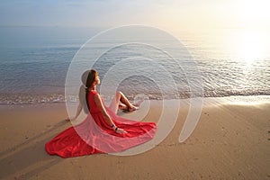 Lonely young woman sitting on ocean sandy beach by seaside enjoying warm tropical evening