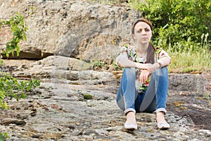 Lonely young woman sitting on rocks