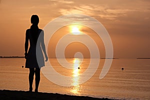 Lonely young woman standing on ocean beach by seaside enjoying warm tropical evening
