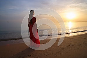 Lonely young woman standing on ocean beach by seaside enjoying warm tropical evening