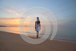 Lonely young woman standing on sandy beach by seaside enjoying warm tropical evening