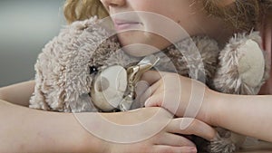Lonesome child with teddy bear waiting for parents to take her from orphanage