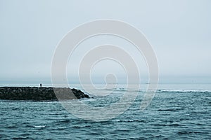 Lonesome person standing on the rocky surface of Atlantic Ocean`s coastline in Iceland