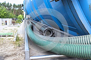 Long 4 inch PVC suction hoses lie next to the tank of the septic tank truck.
